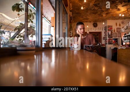 Junge Frau liest Magazin in einem kleinen Café und genießt Ihr Getränk Stockfoto