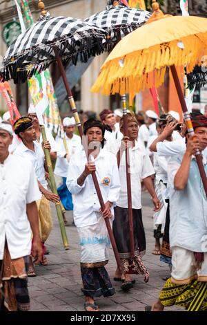 Galungan Urlaub. Festliche Prozession der Männer mit Regenschirmen in den Händen. Bali, Indonesien. 26.12.2018 Vertikale Ausrichtung Stockfoto