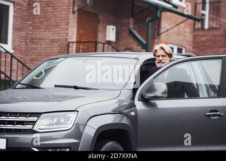 Modischer älterer Mann mit grauen Haaren und Bart ist im Freien Auf der Straße, die in seinem Auto sitzt Stockfoto