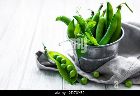 Frische grüne Erbsen in einem kleinen Metalleimer auf alt Holzhintergrund Stockfoto