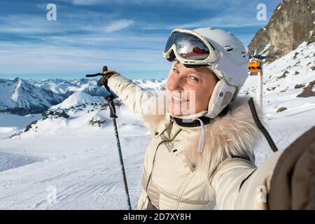 Junge Erwachsene schöne glücklich attraktive kaukasische lächelnde Skifahrer Frau Porträt machen Selfie auf Berggipfel zeigt Skigebiet Panorama Stockfoto