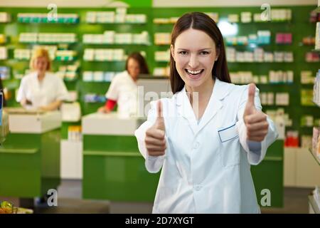 Der lachende Apotheker in der Apotheke hält beide Daumen hoch Stockfoto