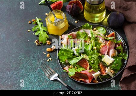 Gesunde Ernährung Konzept. Herbstsalat mit Feigen, Prosciutto, Rucola, Spinat, Käse, Walnüssen und Honig auf einer Steinplatte. Speicherplatz kopieren. Stockfoto
