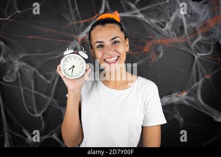 Junge schöne Frau auf schwarzem Hintergrund mit Spinnweben und Spinnen Lächelnd und mit einer Uhr Stockfoto