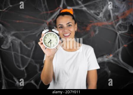 Junge schöne Frau auf schwarzem Hintergrund mit Spinnweben und Spinnen Lächelnd und mit einer Uhr Stockfoto