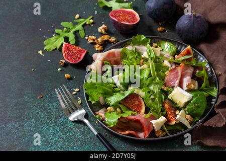 Gesunde Ernährung Konzept. Herbstsalat mit Feigen, Prosciutto, Rucola, Spinat, Käse, Walnüssen und Honig auf einer Steinplatte. Speicherplatz kopieren. Stockfoto