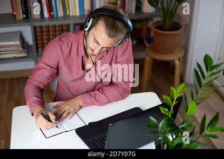 Hübscher junger kaukasischer Mann, der Computer benutzt, der zu Hause arbeitet und Mit Kopfhörern sprechen und sich glücklich fühlen Stockfoto