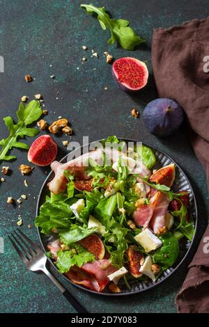 Gesunde Ernährung Konzept. Herbstsalat mit Feigen, Prosciutto, Rucola, Spinat, Käse, Walnüssen und Honig auf einer Steinplatte. Draufsicht flach liegend Rückenlage Stockfoto