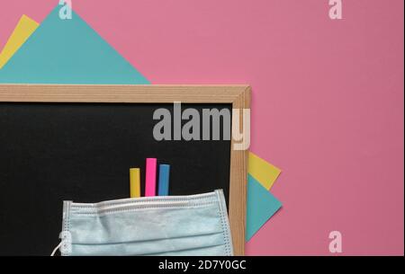 Gesichtsmaske auf schwarzen Brett, Malstift und Papier. Rosa Hintergrund, Draufsicht. Speicherplatz kopieren. Stockfoto