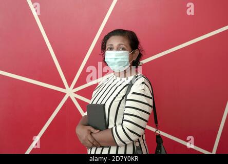 Porträt der Geschäftsfrau trägt Gesichtsmaske, hält ein Tagebuch. Roter Hintergrund. Stockfoto