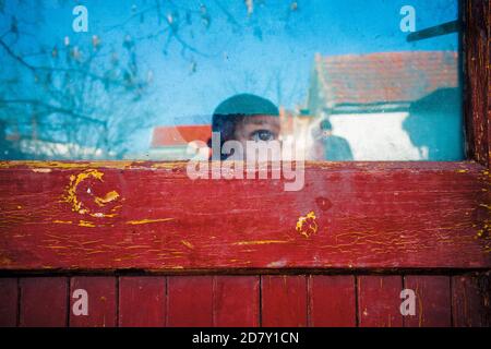 Kind, das furchteinflößend durch ein Fenster schaut Stockfoto