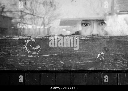 Schwarz-Weiß-Bild eines Kindes, das furchteinflößend durchschaut Ein Fenster Stockfoto