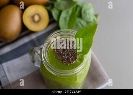 Grüner Smoothie mit Chia im Einmachglas auf grauem Hintergrund mit Kiwis und Spinat.Detox-Cocktail, gesundes Diätkonzept mit Spinat, Ananas, Kiwi und Stockfoto