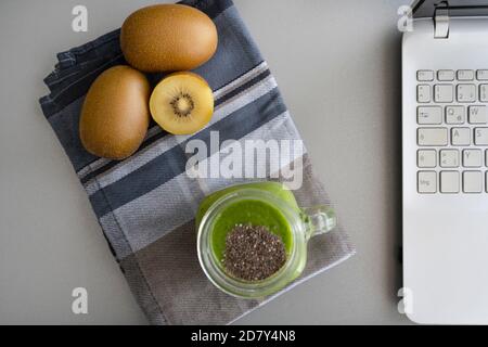 Gesunder Arbeitsplatz mit grünem Smoothie und Laptop auf grauem Hintergrund mit kiwis.work zu Hause, Zeitpause, freiberuflicher und digitaler Nomadenkonzept. Stockfoto