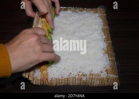 Chef Hände machen Sushi-Rolle, Reis mit Avocado und gebratene Garnelen.Japanisches Essen Konzept. Stockfoto