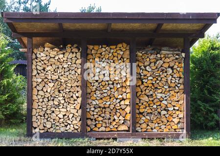 Sie bereiten Brennholz für die Heizung im Winter. Brennholz wird ordentlich unter dem Dach des Schuppen zum Heizen gestapelt. Stockfoto