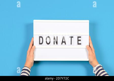 Hände halten Leuchtkasten mit Donate Wort Text über hellblauen Hintergrund. Draufsicht Stockfoto