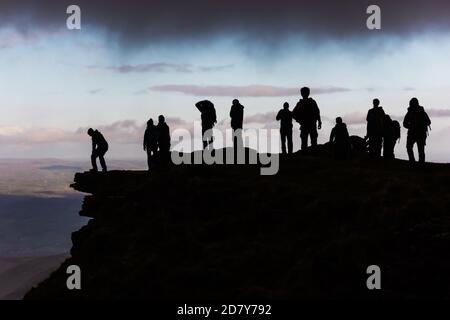 Schwarze Silhouetten von Wanderern auf der Spitze eines Berges, der nach einem Bergsteigen unter einer grauen Wolke ruht. Stockfoto