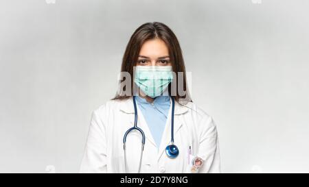 Weibliche junge Arzt gefaltet Hände mit Schutz medizinische Maske, Stethoskop über Hals und weißem Mantel. Covid 19, Coronavirus, Healthcare Concept Banner. Stockfoto