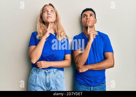 Junge interracial Paar tragen lässige Kleidung Denken konzentriert über Zweifel Mit Finger am Kinn und Blick nach oben wundernd Stockfoto
