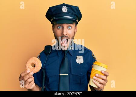 Gutaussehende hispanische Polizei Mann essen Donut und trinken Kaffee feiern verrückt und erstaunt für den Erfolg mit offenen Augen schreien aufgeregt. Stockfoto