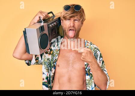 Junge blonde Mann trägt Sommer-Stil halten Boom Box aufragend Zunge aus glücklich mit lustigen Ausdruck. Stockfoto