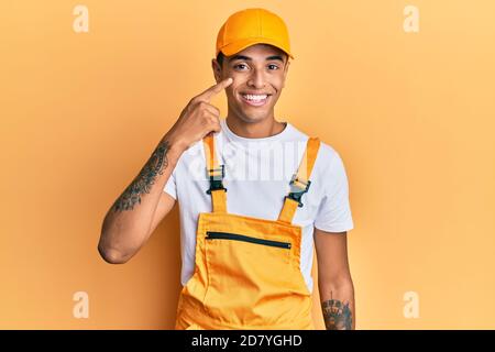 Junger schöner afroamerikanischer Mann trägt Handyman Uniform über gelbem Hintergrund zeigt mit Hand Finger zu Gesicht und Nase, lächelnd fröhlich. beau Stockfoto