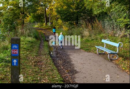 River Tyne, Haddington, East Lothian, Schottland, Großbritannien, 26. Oktober 2020. UK Wetter: Herbstfarben: Sonnenschein zusammen mit Herbstblättern beleuchtet in der Sonne, als zwei kleine Mädchen auf dem Uferwanderweg, der auch Radroute 196 ist, Roller fahren Stockfoto