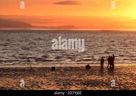 Prestwick, Ayrshire, Schottland, Großbritannien. Fischer genießen den Sonnenuntergang am Firth of Clyde mit Blick auf die Insel Arran. Ayr, Ayrshire, Schottland. Sept 2015 . Schattenmenschen mit Hund genießen einen abendlichen Spaziergang am Strand von Ayr entlang, während die Sonnenuntergänge über der Insel Arran. Platz für Text oder Text Stockfoto