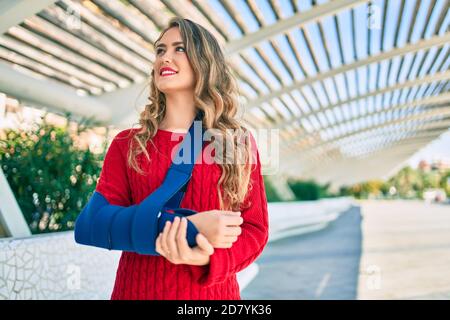 Junge blonde Mädchen lächelnd glücklich verletzt mit Arm Sling stehen im Park. Stockfoto