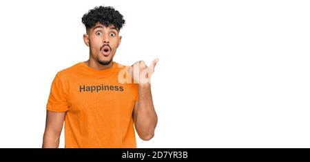 Junger arabischer Mann trägt T-Shirt mit Glück Wort Nachricht überrascht zeigt mit Handfinger zur Seite, offenen Mund erstaunt Ausdruck. Stockfoto