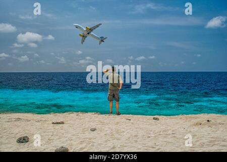 Mann am karibischen Strand, der Flugzeuge ansieht, die sich in der Stadt aufmachen Die Luft über einem blauen Ozean Stockfoto