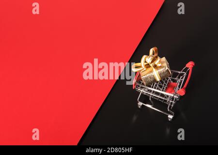 Goldene Geschenkbox und Warenkorb auf schwarz rotem Hintergrund. Angebot „Black friday“ Stockfoto