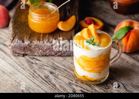 Pfirsichfrucht Dessert in Glas Tasse auf Holztisch. Hausgemachtes Dessert mit Früchten. Obstsalat mit Joghurt oder Sauerrahm. Stockfoto