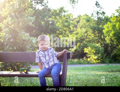 Kleinkind Junge auf einer Bank mit einem Spielzeug Traktor Stockfoto