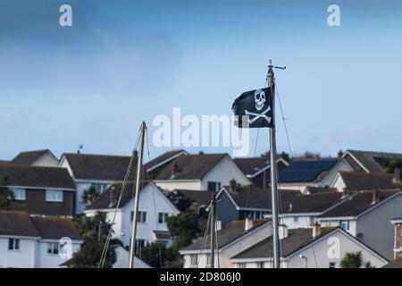 Eine Skull- und Crossbones-Flagge flattert vom Mast eines Bootes mit Küsteneigentum im Hintergrund. Stockfoto