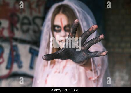 Horror, Alptraum und Halloween Konzept. Tote Braut. Junge Frau im Zombie Make-up mit Braut Schleier auf dem Kopf schaut in die Kamera reichen ihre Hand f Stockfoto