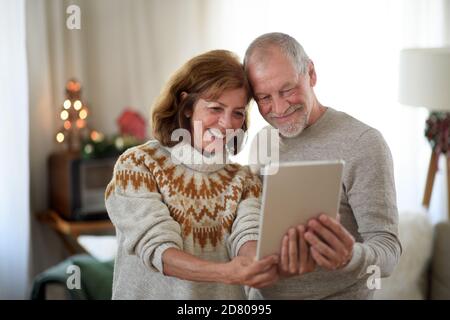 Vorderansicht des älteren Paares mit Tablet drinnen zu Hause zu Weihnachten, Selfie zu nehmen. Stockfoto