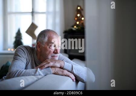 Einsamer älterer Mann sitzt auf dem Sofa drinnen zu Weihnachten, Einsamkeit Konzept. Stockfoto