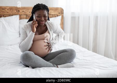 Afroamerikanische Schwangere Dame, Die Schmerzen Im Bauch Fühlt, Ruft Arzt Auf Dem Handy Stockfoto