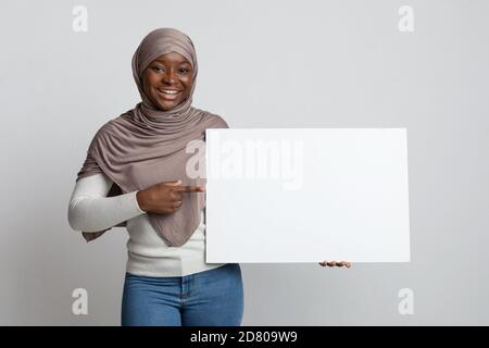 Glückliche afrikanische muslimische Frau in Hijab zeigt auf weißes Plakat In Händen Stockfoto