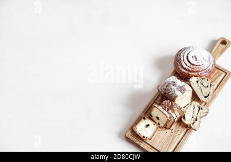 Verschiedene frische Backwaren werden auf einem Holzstab geschnitten. Auf einem hellen Hintergrund Platz für Text. Stockfoto