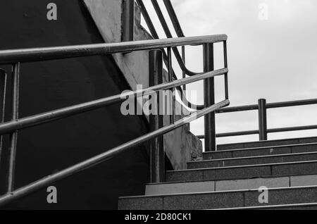 Treppe mit Geländer draußen. Schwarz-Weiß-Foto einer Steintreppe mit Metallgeländer. Ohne irgendjemanden. Stockfoto
