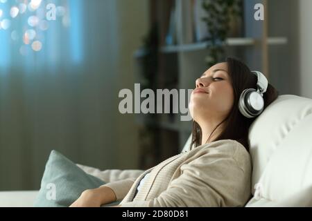 Entspannte Frau sitzt auf einem Sofa und hört Musik Die Nacht zu Hause Stockfoto