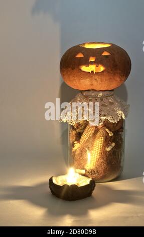 jack o Laterne auf großen Glas getrockneten Mais auf der Kohle und Maisseide. Am Kerzenhalter mit einer brennenden Kerze. Geheimnisvolle Schatten Stockfoto