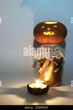 jack o Laterne auf großen Glas getrockneten Mais auf dem Kob und Mais Stigmas. Am Kerzenhalter mit einer brennenden Kerze. Geheimnisvolle Schatten Stockfoto