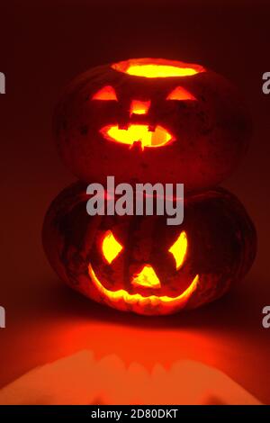 halloween Kürbis auf anderen halloween Kürbis. Geheimnisvolle rote Beleuchtung und Reflexionen. Geschnitzte gruselige Gesichter Stockfoto