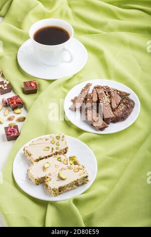Traditionelle arabische Süßigkeiten Sesam Halva mit Schokolade und Pistazie und eine Tasse Kaffee auf grünem Textilhintergrund. Seitenansicht, Nahaufnahme. Stockfoto