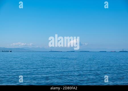 Drapetsona alter Hafen, Piräus, Griechenland. Frachtschiffe und Boote. Blick vom Strand auf festfahrende Schiffe. Blauer Himmel und klares ruhiges Meer ein sonniger Tag. Stockfoto