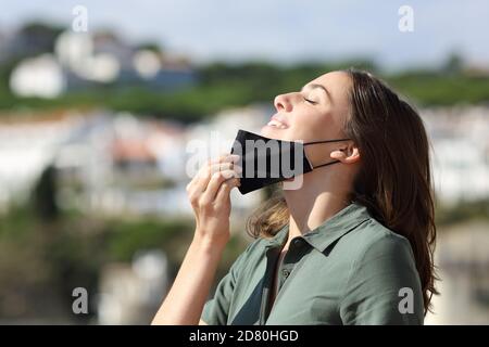 Seitenansicht Porträt einer glücklichen Frau, die frische Luft atmet Entfernen von Maske in einer ländlichen Stadt Stockfoto